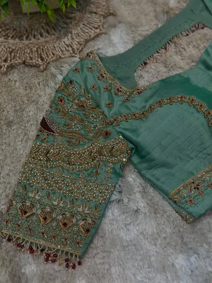 A close-up of the sleeve of the pastel green blouse, showcasing the dense zardosi, bead, and stonework.