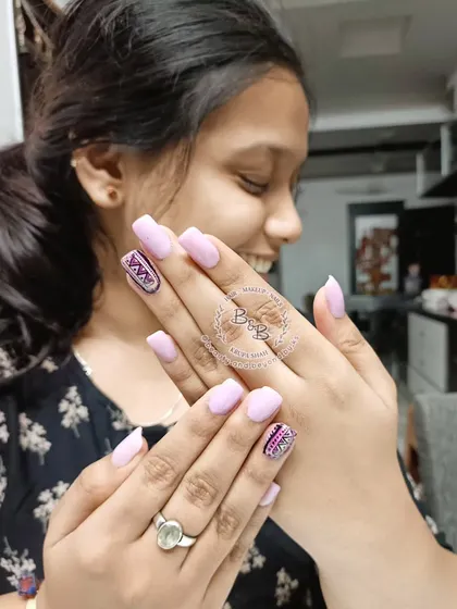 This client is happily showing off her short form nail extensions. The design features a soft pink base with geometric foil art and glitter accents on the ring fingers for a modern, artistic touch.