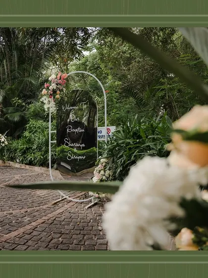 A beautifully framed shot of the welcome sign, seen through the lush foliage of the venue, emphasizing the integration of decor and nature.