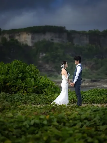 A quiet moment of connection amidst the lush greenery of a Bali beach. The contrast between the vibrant foliage and the distant cliffs adds depth to this destination portrait.