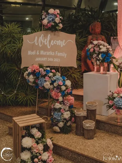 A rustic yet chic welcome sign. The simple wooden board is elevated by a cascade of beautiful pink, blue, and white flowers, creating a stunning welcome piece.