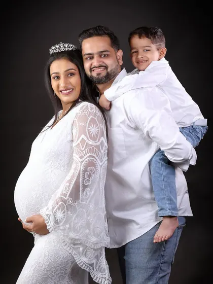 A joyful family pose with the son getting a piggyback ride from his dad. Everyone is smiling, capturing the happy and exciting atmosphere of waiting for the new baby.