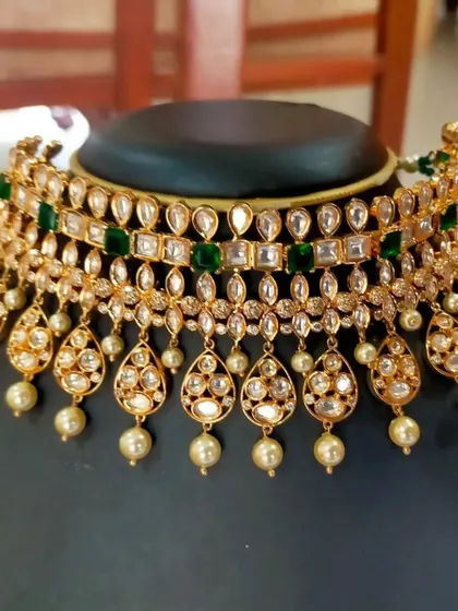 This layered Kundan choker with pearl drops is a classic design. The green stones add a touch of color, making it a sophisticated choice for weddings and formal events.