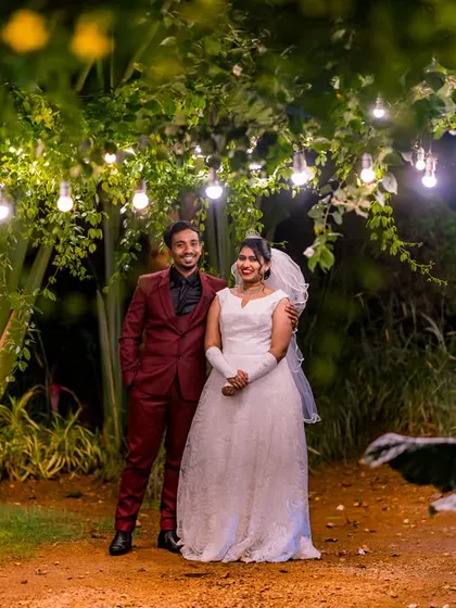 A full-length portrait of a couple in their fairy-tale outfits, standing in a garden path lit by hanging bulbs. This shot captures the magical ambiance of the entire scene.