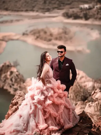 For pre-wedding shoots, I love finding epic locations like this one. The couple stands on a rocky cliff overlooking the water, creating a truly breathtaking and romantic image. The stunning pink ruffled gown is from my rental collection.