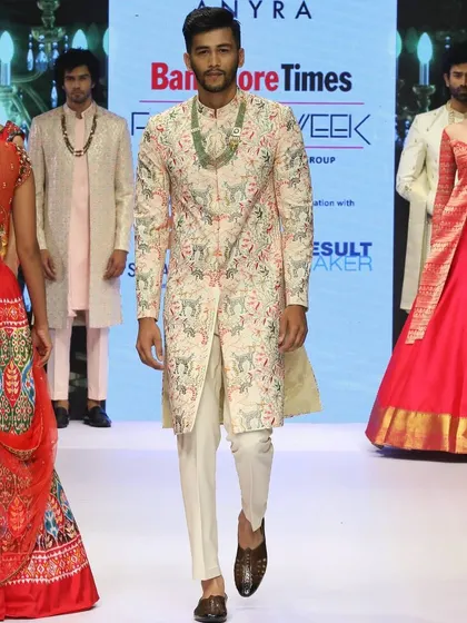 Another view of the light pink embroidered sherwani from the fashion week runway. You can see how it is styled with simple white trousers to keep the focus on the jacket's detailed craftsmanship.