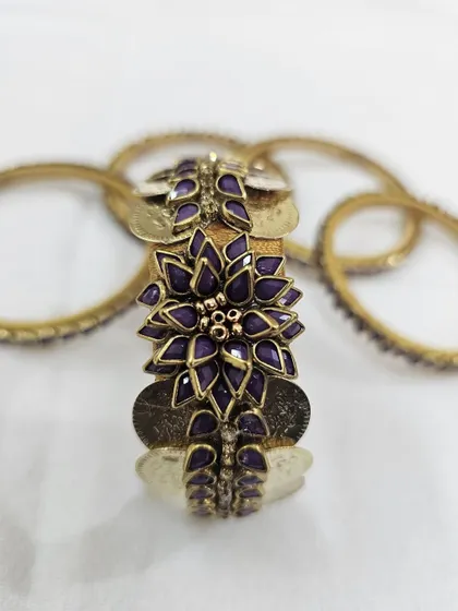A close-up of the central floral kundan piece on the purple silk thread bangle set.