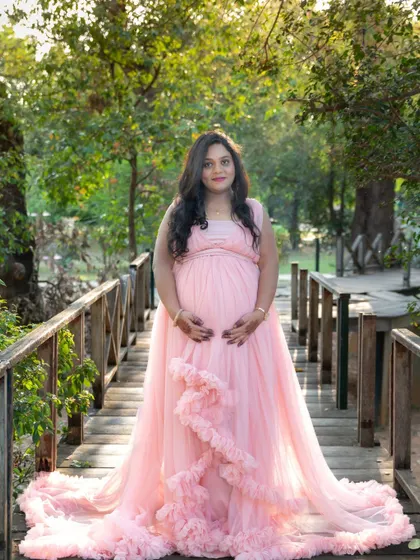 A beautiful portrait of a mom-to-be on a wooden bridge in a park, wearing a lovely pink ruffled gown.