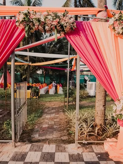 A welcoming entrance for a vibrant outdoor event, using bright orange and pink drapes with floral accents to set a cheerful tone.