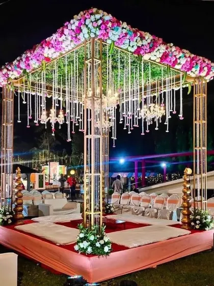 A modern mandap design with a metallic gold frame, a canopy of pink and blue flowers, and hanging crystal strings. This is a perfect blend of contemporary structure and classic floral elegance.