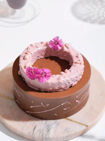 A close-up of the Belgian Chocolate and Raspberry Entremet, focusing on the textured raspberry ring and delicate flower garnish.