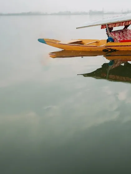 An atmospheric shot of a lone Shikara boat on the misty waters of Dal Lake, setting the scene for a romantic Kashmir story.