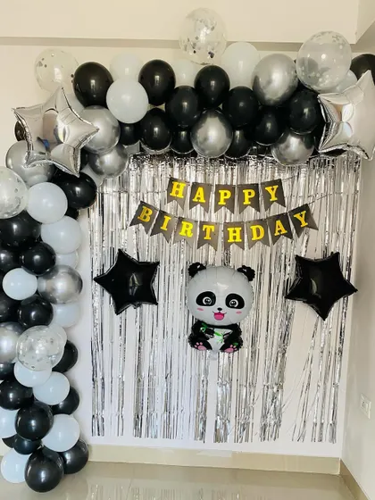 A panda-themed birthday backdrop with a black, white, and silver balloon arch over a foil curtain.