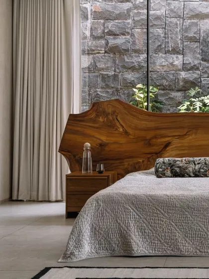 A detail of the master bedroom, where the raw wood headboard meets the large window overlooking a private court. The design is all about creating a direct and immersive connection with nature.