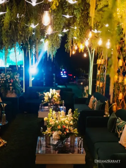 A luxurious lounge area with plush emerald green sofas set under a ceiling of cascading foliage and hanging lights. We design these comfortable yet stylish spaces for guests to relax and socialize.
