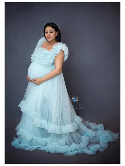 A beautiful solo portrait of the mother-to-be, cradling her baby bump in an elegant blue gown, radiating grace and happiness.
