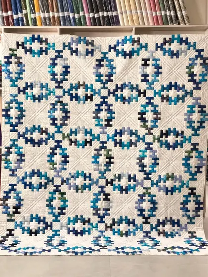 A beautiful "Summer Wedding Ring" quilt, a modern take on the classic double wedding ring. The intricate blue and teal pattern is set against a white background with detailed ruler work quilting.