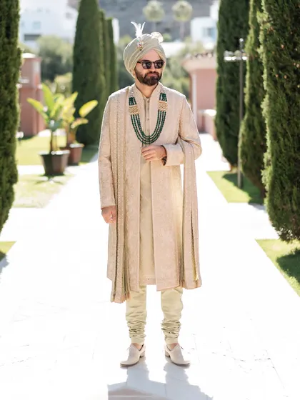 A full-length portrait of the groom in his sage green Tarun Tahiliani sherwani. The emerald neckpiece adds a perfect pop of color, breaking the monotony of the pastel look.