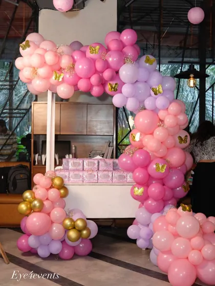 A custom candy cart decorated with a pink and lilac balloon arch with gold butterfly accents. This serves as a beautiful and functional piece, perfect for displaying treats or party favors at a baby shower.