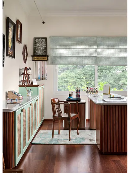 The paint studio is a bright, inspiring space with mint green and wood cabinets, a large quartz work island, and walls adorned with the resident's own intricate Tanjore paintings.
