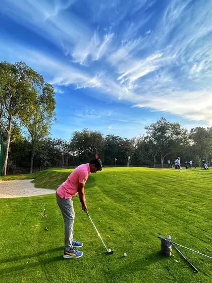A golfer practices their short game on the chipping green under a stunning blue sky with wispy clouds. It's a perfect day for golf.