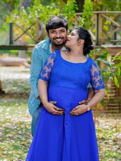 A sweet and playful moment between a couple in a park. The partner's kiss on the cheek and their hands on the baby bump create a photo full of love and happiness.