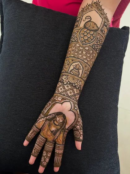 A full-arm design that incorporates a bride portrait, a peacock, and a traditional pot (kalash) motif.