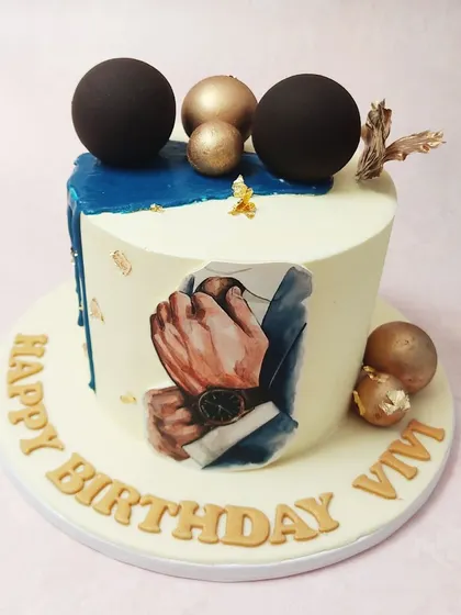We design a cake for the modern gentleman. This sophisticated birthday cake features a painted image of a man adjusting his suit, complemented by a deep blue drip, gold leaf, and dark, elegant spheres for a truly distinguished look.