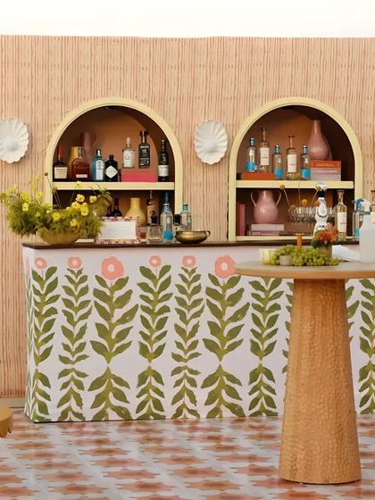 A custom-designed bar with a whimsical botanical print and a rattan-textured facade. The arched back-bar shelving adds a touch of architectural charm.