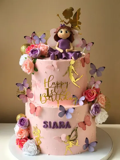 A beautiful two-tiered cake with a fairy theme, decorated with flowers, butterflies, and a custom doll topper.
