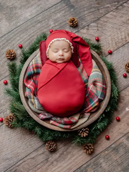 Another perspective of the Christmas wreath setup, showcasing the baby's festive red wrap and the beautiful texture of the wooden floor.