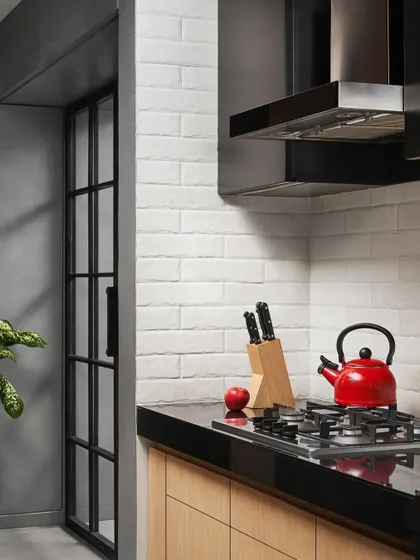 A pop of red from a kettle adds a playful touch to the otherwise monochrome kitchen. The white subway tile backsplash provides a clean, classic backdrop for the black granite countertops.