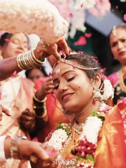 A beautiful close-up of a bride during a South Indian wedding ritual. The groom's hand places the sacred 'jeelakarra bellam' on her head, and her blissful smile captures the emotion of the moment.
