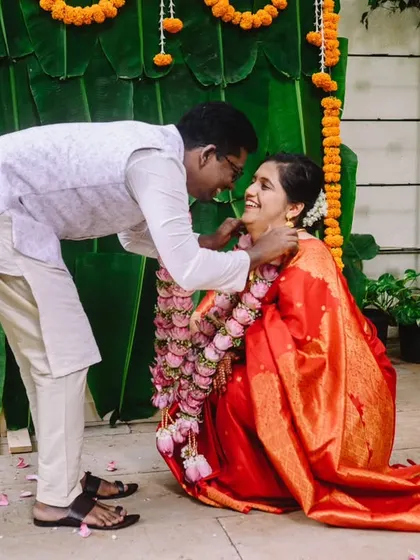 A close up of the varmala exchange. The groom leans in to place the garland, and the bride's expression is full of happiness. An intimate moment from their close knit wedding.
