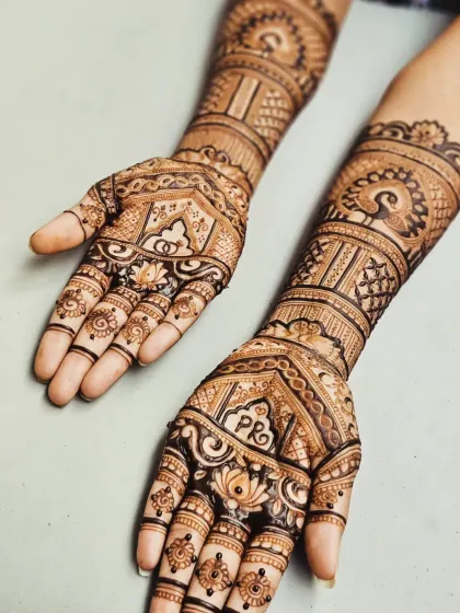 This engagement mehendi combines traditional peacock and lotus elements with personalized initials. The intricate patterns on the arms complement the detailed work on the palms.