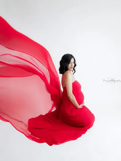 A dynamic and powerful portrait. The flowing red fabric creates a sense of movement and drama, highlighting the mom-to-be's confident pose.