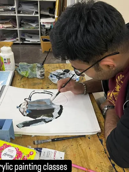 A student concentrates on a monochrome still life painting. This focused practice is key to mastering the fundamentals of light, shadow, and form.