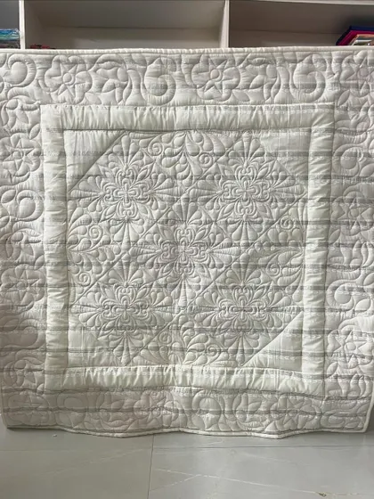 An all-white beginner baby quilt that showcases the beauty of intricate longarm quilting. The complex floral and geometric stitching adds incredible texture.