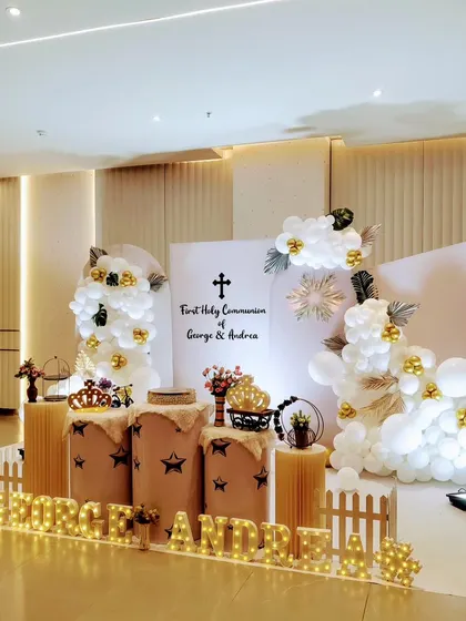 Another angle of the elegant First Holy Communion decor, showcasing the clean lines of the backdrop and the thoughtful placement of decorative elements like crowns and a miniature bicycle.