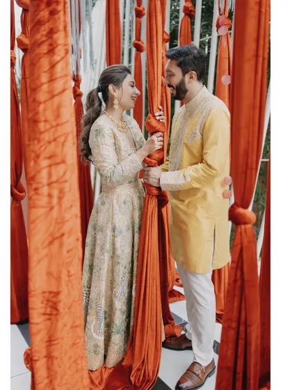 A playful moment between the couple amidst vibrant orange drapes, part of their Haldi ceremony decor.