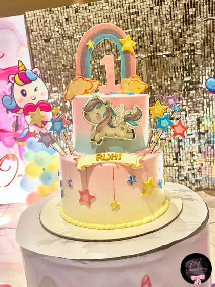 A close-up of the custom two-tier cake for a unicorn-themed party. The cake is decorated with a flying unicorn, stars, and a rainbow, perfectly matching the overall party decor.