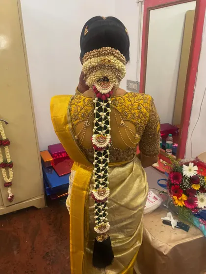 A traditional bridal braid adorned with fresh flowers and a full set of 'Jadai'. This look is perfect for a morning wedding ceremony, photographed in a home setting.