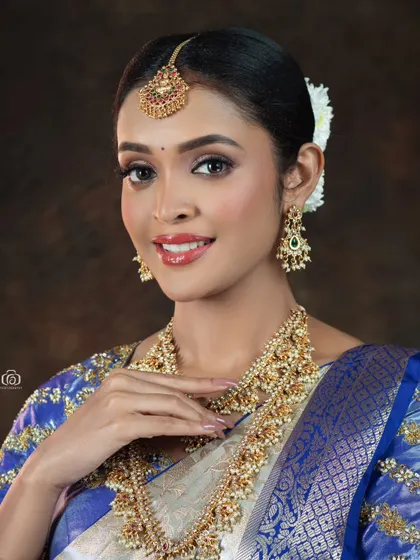 A close-up beauty shot focusing on the model's joyful expression and the detailed bridal jewelry. The soft lighting and traditional attire create a classic and timeless portrait.