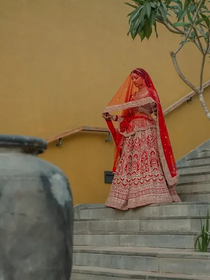 A regal portrait of the couple in their stunning red and cream wedding attire. We use architectural elements like staircases to add a touch of grandeur to our compositions.