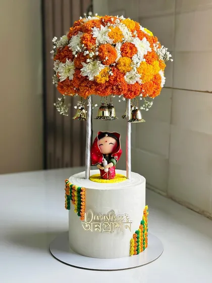 A stunning and unique cake for an Annaprashan ceremony. This design features a beautiful marigold floral arrangement, temple bells, and a cute baby figurine in traditional attire.