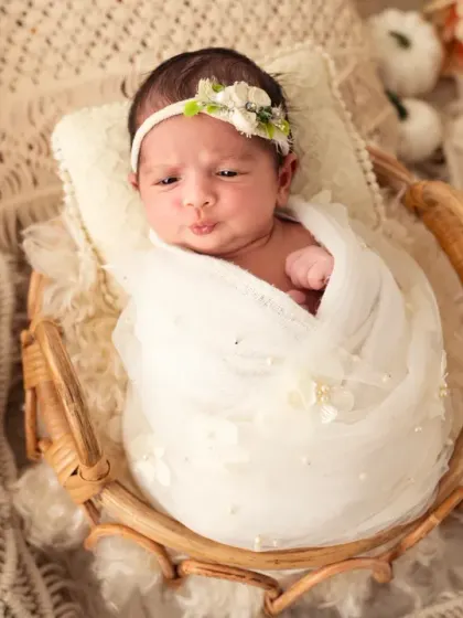 This awake baby girl makes a cute pouty face while wrapped in white and nestled in a boho-style basket.