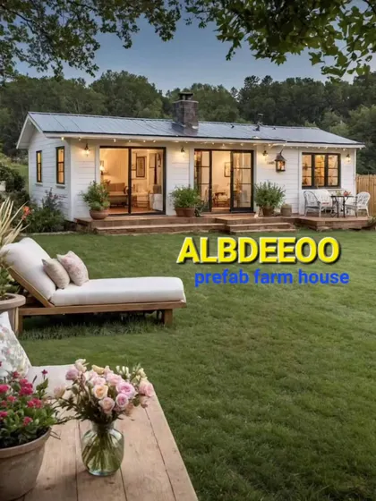 This image captures the dream of a modern prefab farmhouse. The structure features large glass doors that open up to a beautiful lawn, creating a seamless indoor-outdoor living experience.