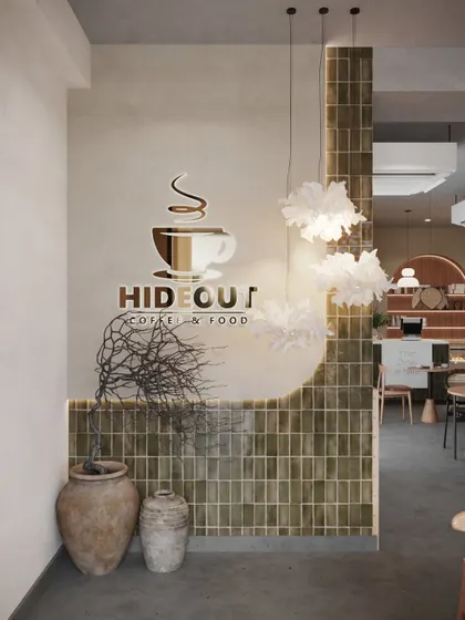 The entrance design for Hideout Cafe sets a sophisticated tone. We used a custom logo decal, unique sculptural decor, and a feature wall of vertically stacked green tiles to create a strong visual identity right at the door.