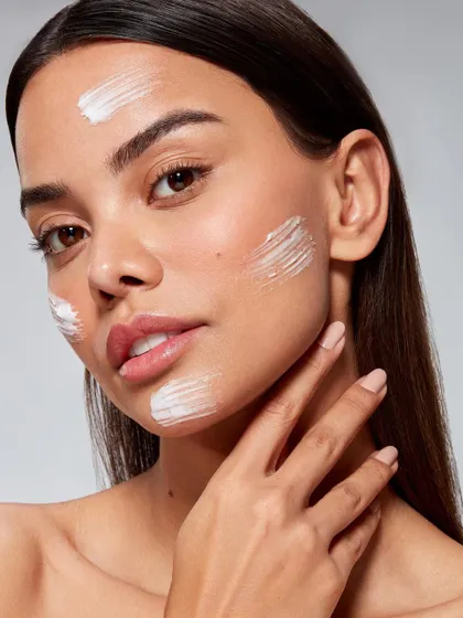 A skincare application shot for Skinora Cosmetics. The image focuses on the texture of a cream product swiped across a model's cheek, highlighting its smooth consistency and feel on the skin.