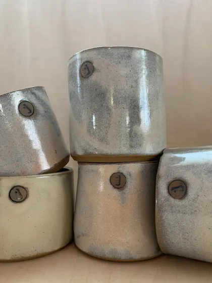 A close-up of the studio cups, showing the beautiful, rustic glaze and the custom stamp.
